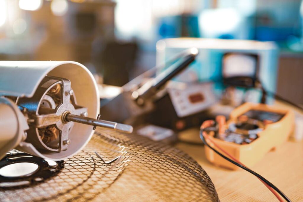 Close-up of an iron motor from home cooling fan and testind tools lies on a table in workshop. The concept of repair and restoration of damaged equipment