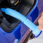 Close up filling of diesel exhaust fluid from canister into the tank of blue car for reduction of air pollution. Environmental or eco friendly solution.