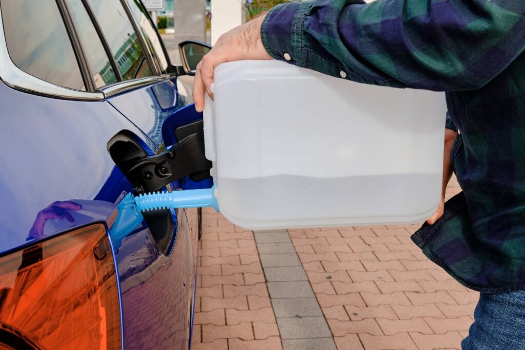 Man filling a diesel engine fluid from canister into the tank of blue car. Diesel exhaust fluid/AdBlue for reduction of air pollution