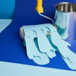 metal shiny can and roller with dripping paper cut paint on bright blue background