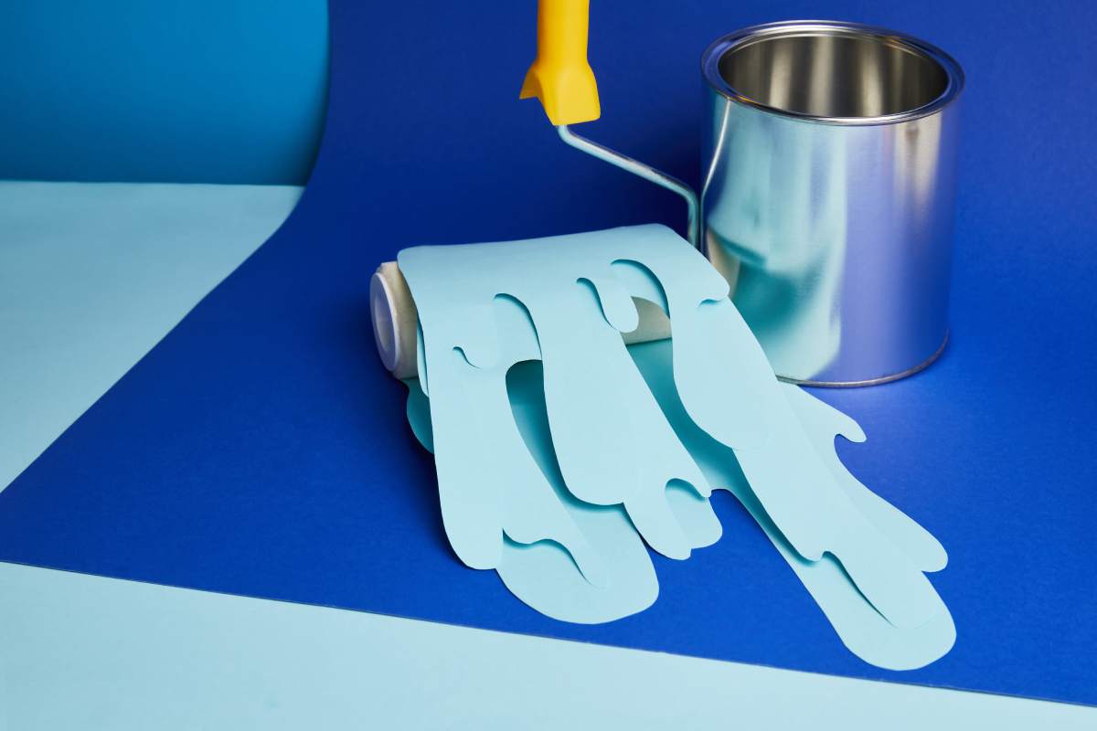 metal shiny can and roller with dripping paper cut paint on bright blue background