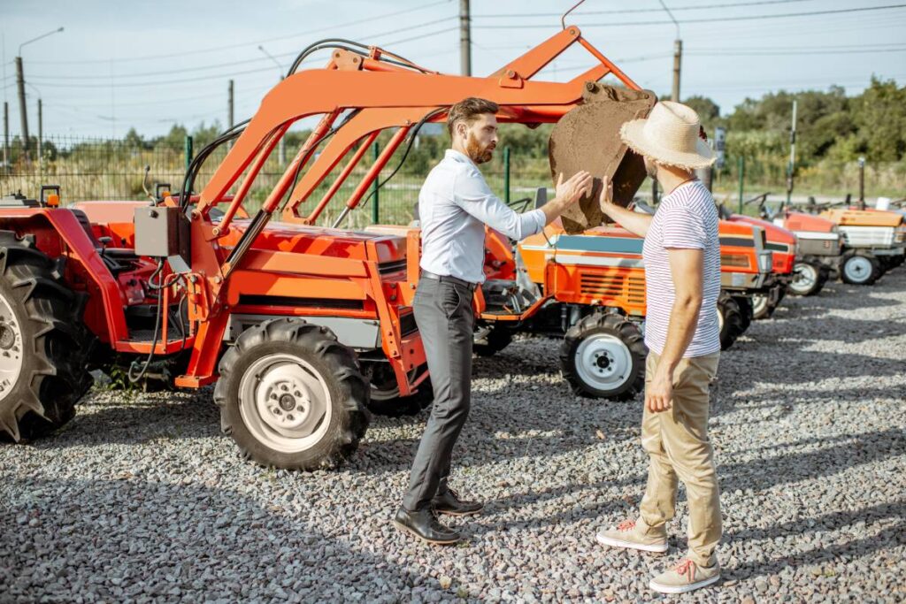 Agronomist choosing a tractor for farming, standing with salesman on the open ground of agricultural shop