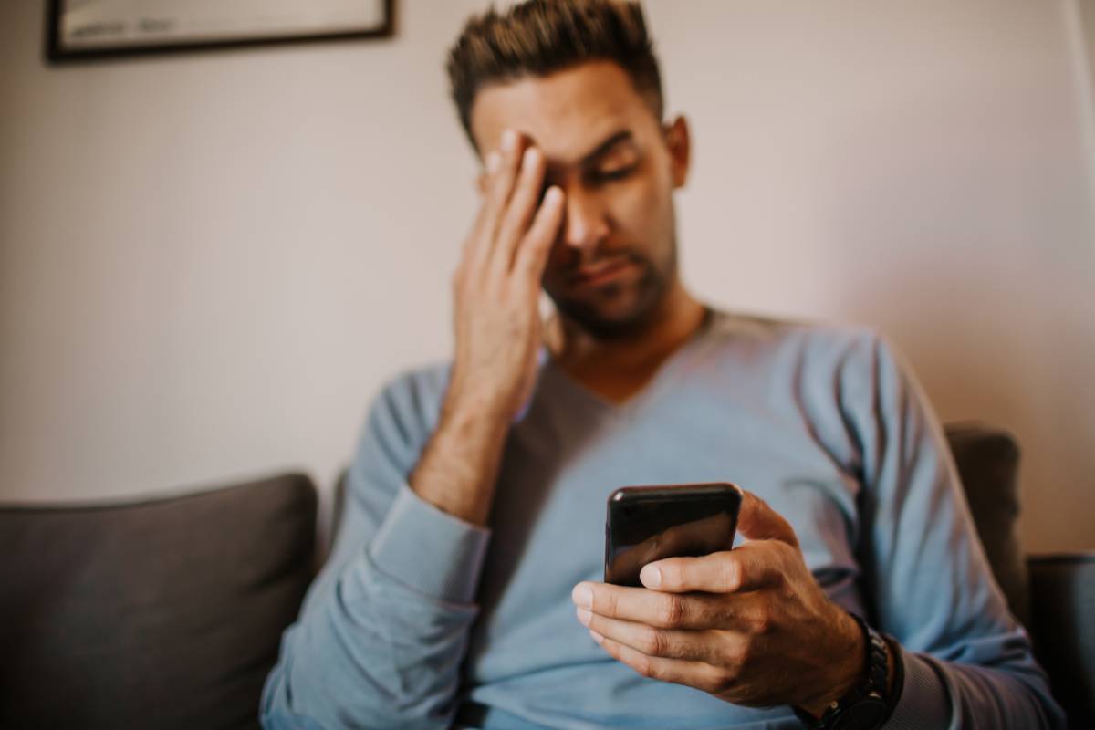 Young handsome man sitting at home on sofa and using mobile phone. Men holding smartphone hands memory